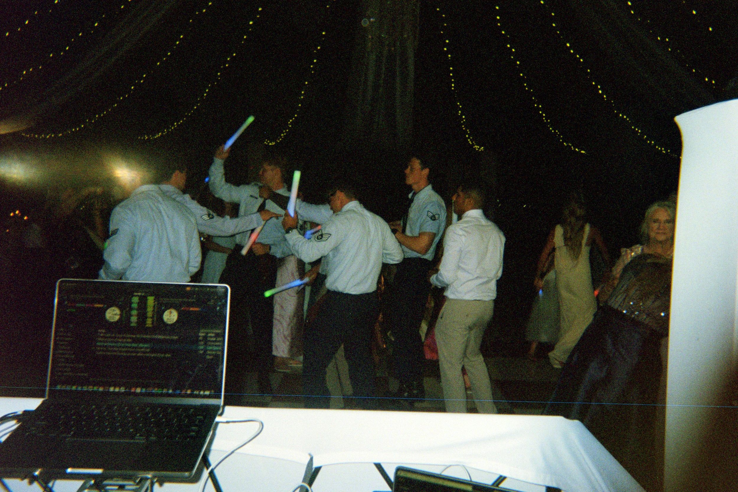 People dancing and enjoying themselves at a dimly lit party or nightclub event with DJ equipment visible.