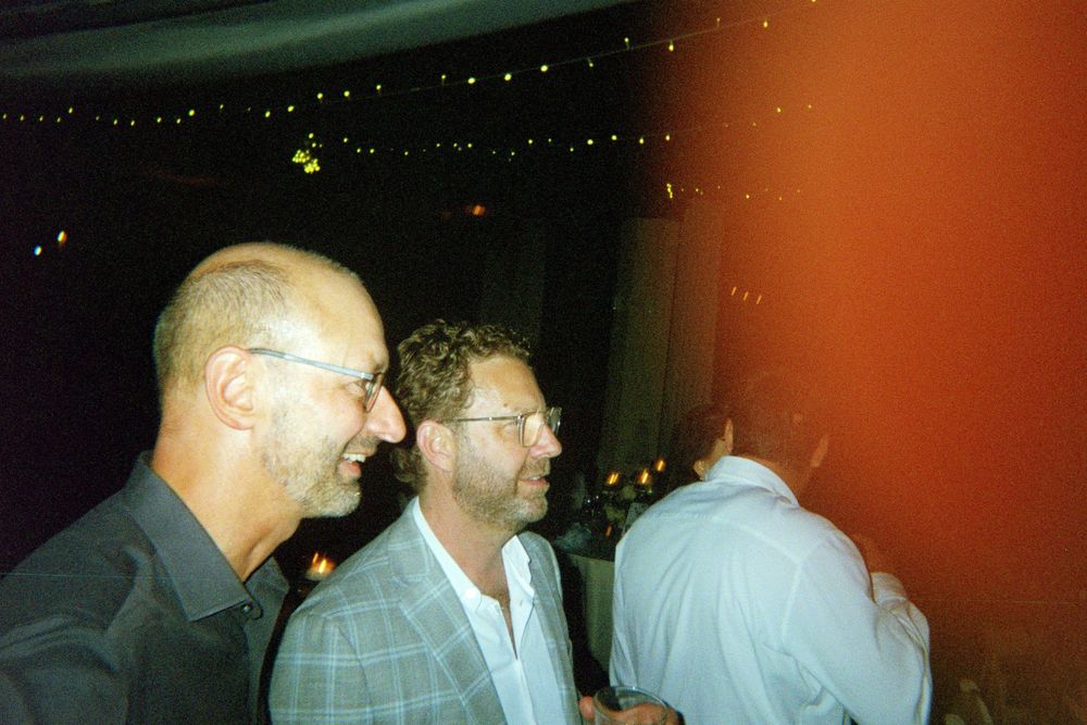 Guests mingling and socializing at an evening event with red ambient lighting in the background.