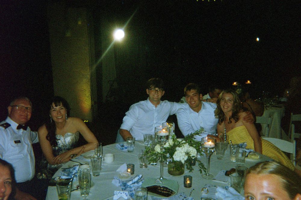 A group of people gathered around a table at an evening outdoor party with table settings and decorative centerpieces.