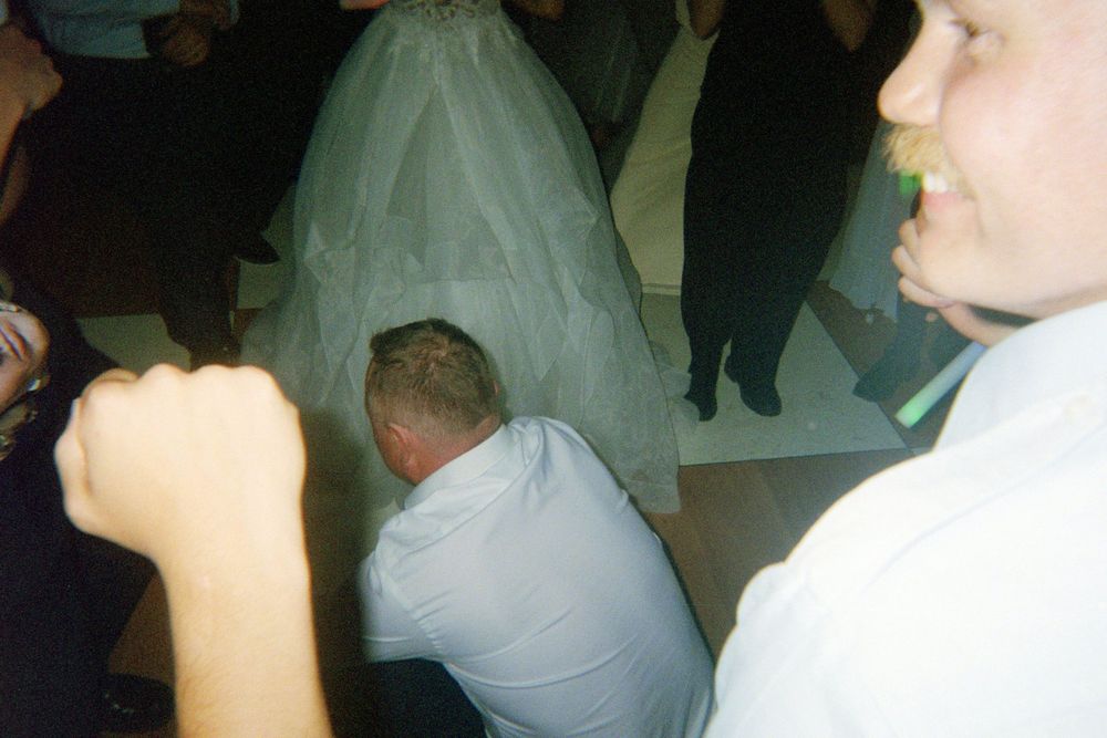 A group of wedding guests dancing and celebrating together on the dance floor at a dimly lit reception.