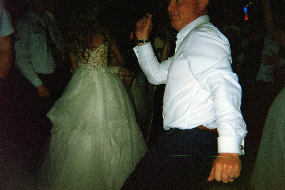Two people in wedding attire dance together at a reception while guests look on.