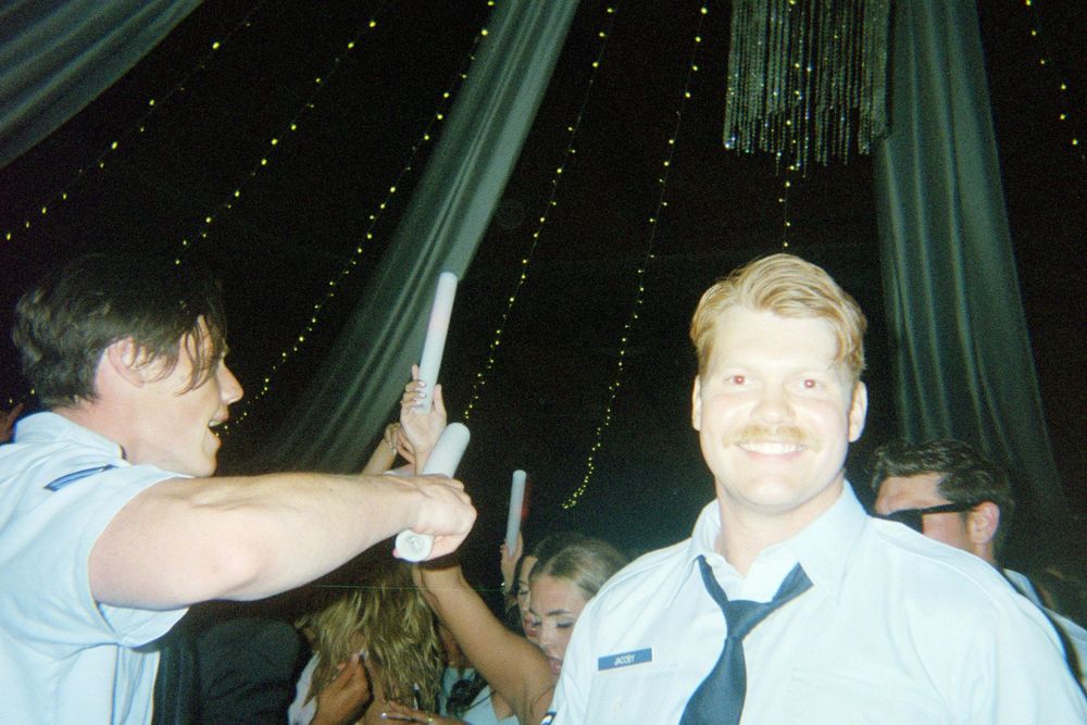 People dancing and celebrating at a party with green draping and twinkling lights in the background.