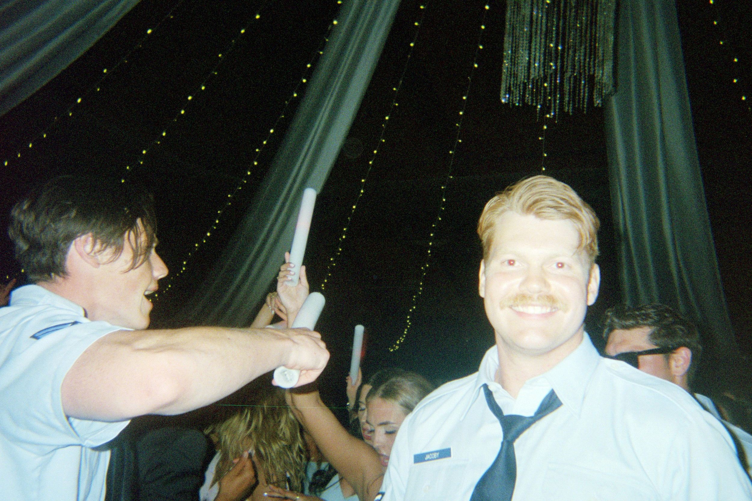 People dancing and celebrating at a party with green draping and twinkling lights in the background.