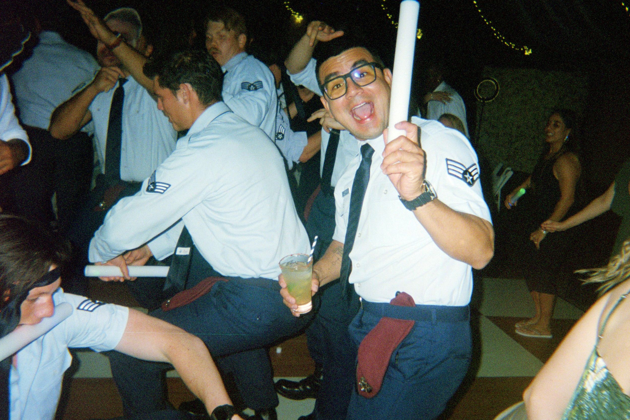 Enthusiastic person in glasses and uniform dances while holding a glowstick at a party.