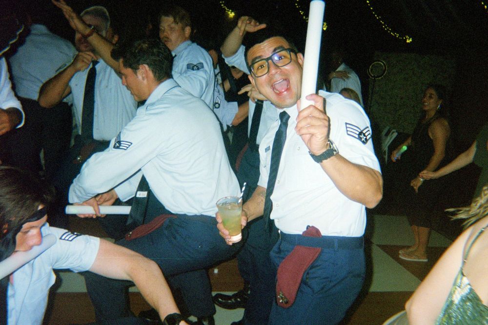 Enthusiastic person in glasses and uniform dances while holding a glowstick at a party.