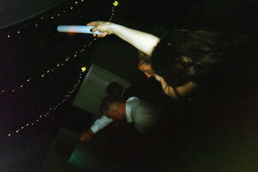 A blurry nighttime photo shows someone performing at a concert with outstretched arms against a dark background with string lights.