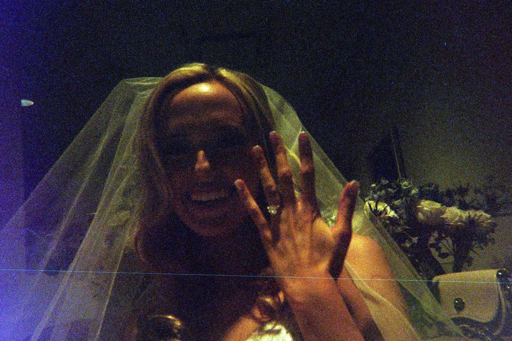 A person wearing a wedding veil holds up their hand showing off their ring under moody lighting.