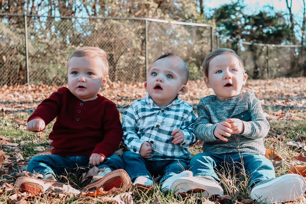 Six children in coordinated outfits sit together outdoors during a fall photoshoot on autumn leaves.
