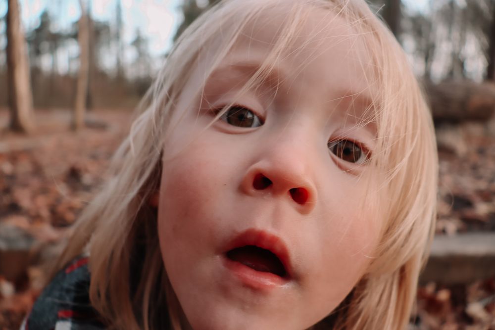 Close up portrait of someone with blonde hair and rosy cheeks looking up at the camera with wonder during autumn.