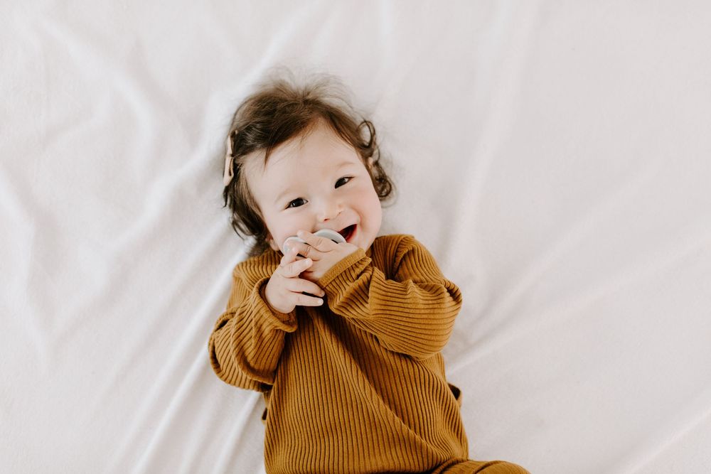 Child wearing a brown knit sweater makes playful expressions while posing against a white background.