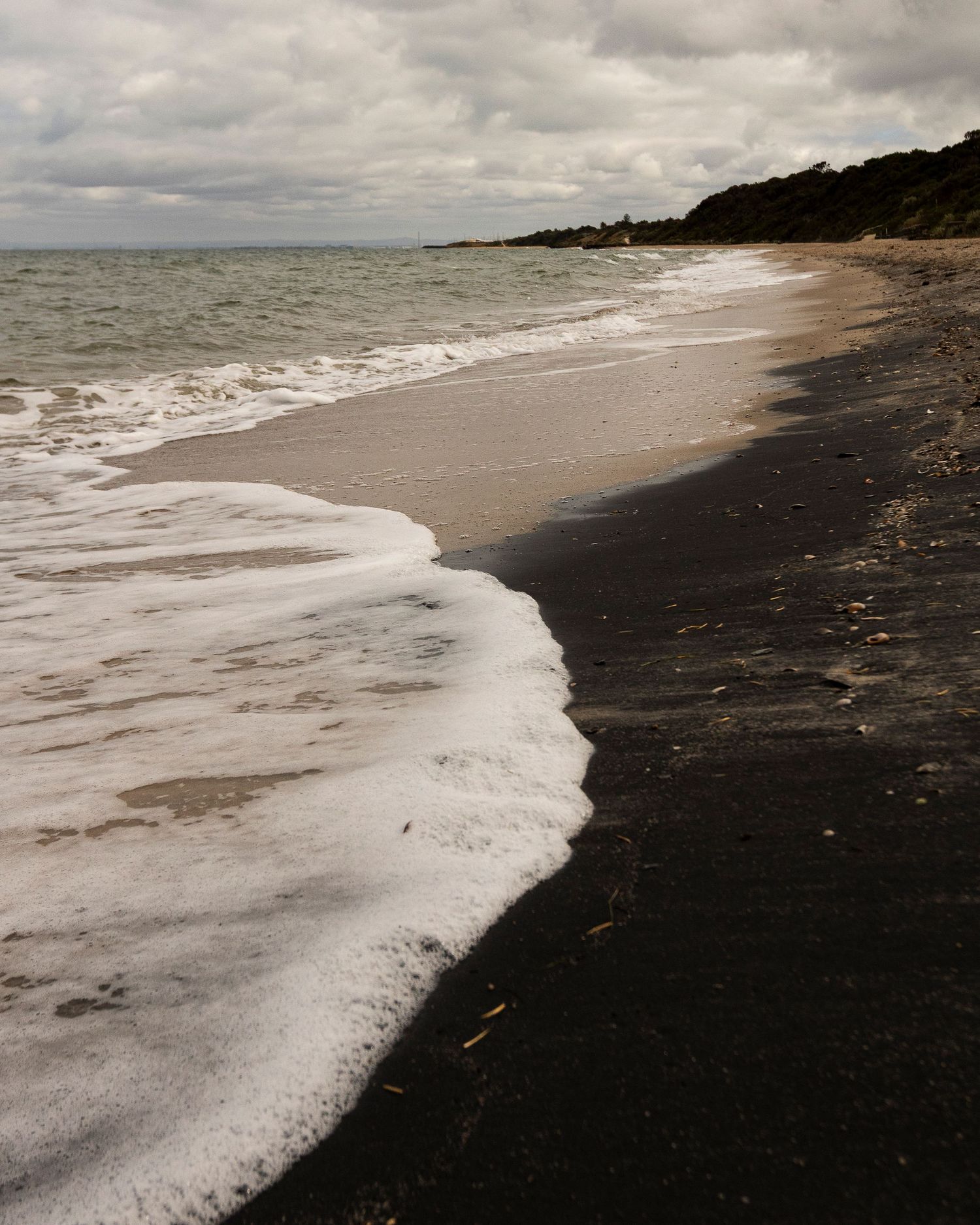 Four images of a dark sandy beach with white foamy waves rolling onto the shore under an overcast sky.
