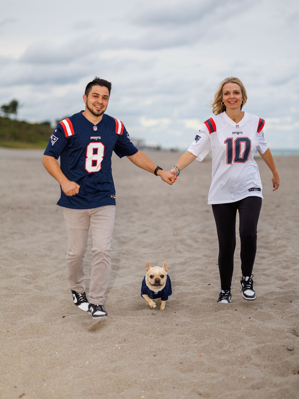 People's legs walking on beach sand wearing sports jerseys.