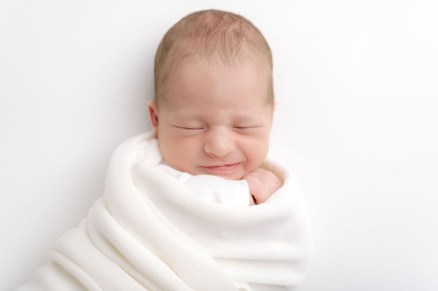 Peaceful sleeping newborn in white knit sweater cuddling with soft beige teddy bear on light background.