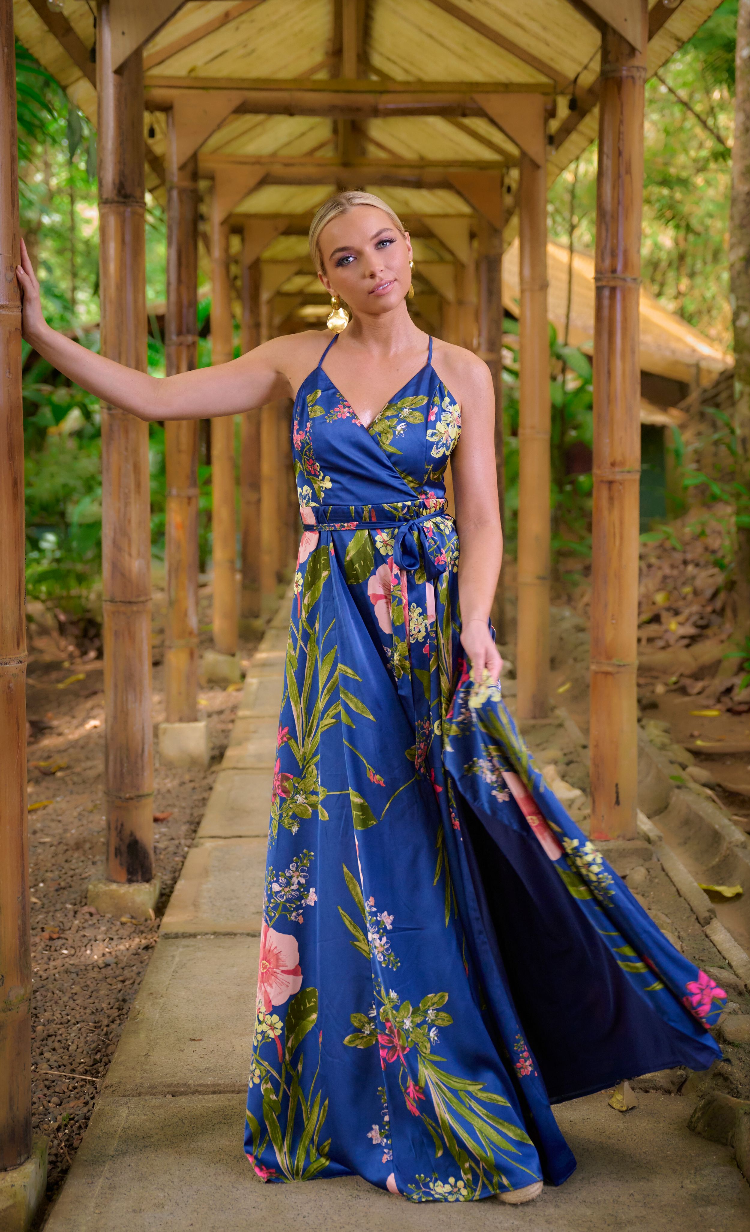 Beautiful floral maxi dress in navy blue with tropical print shown in wooden covered walkway setting.