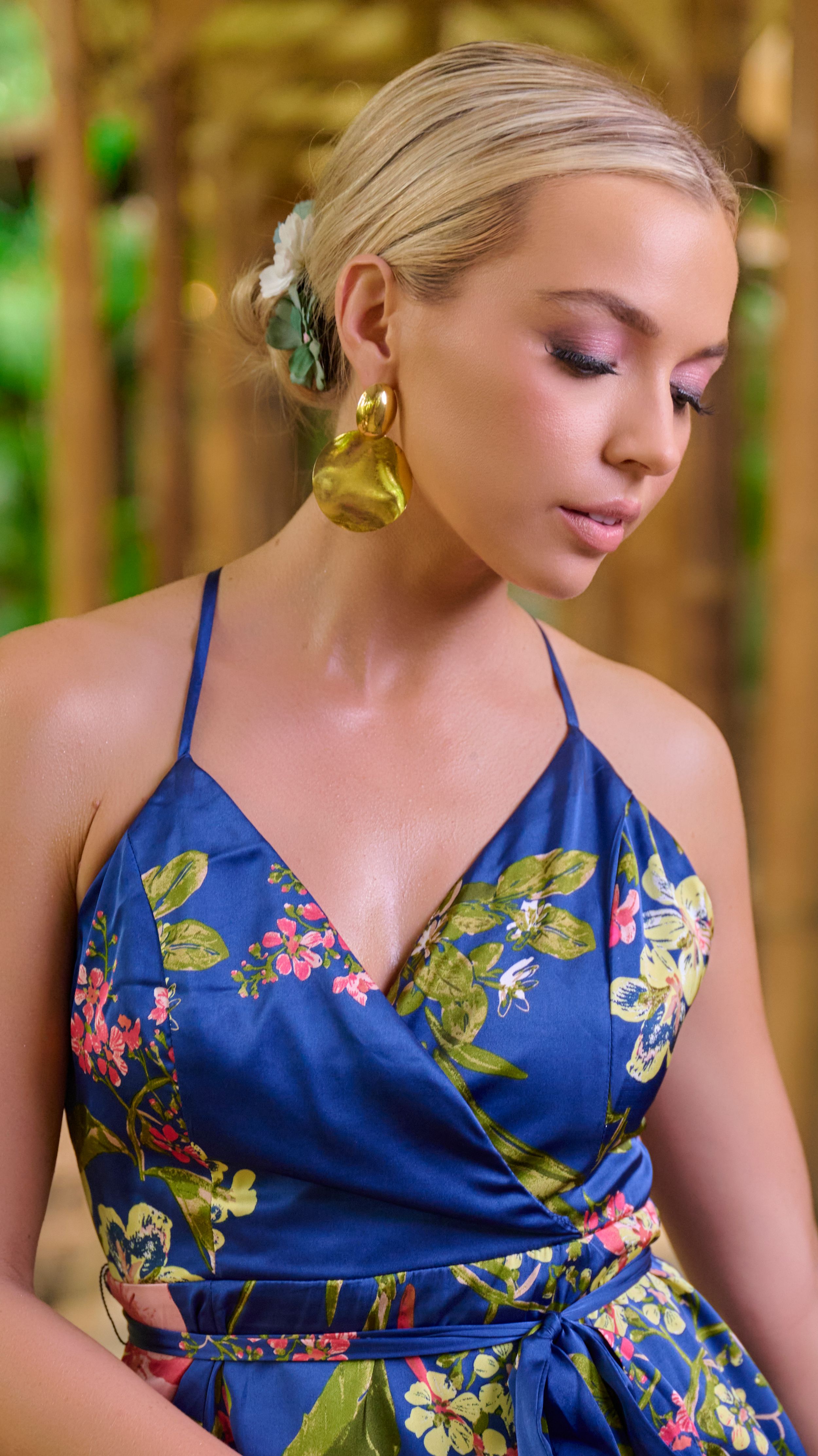 Fashion model wearing a blue floral summer dress in an outdoor garden setting with blurred trees in background.