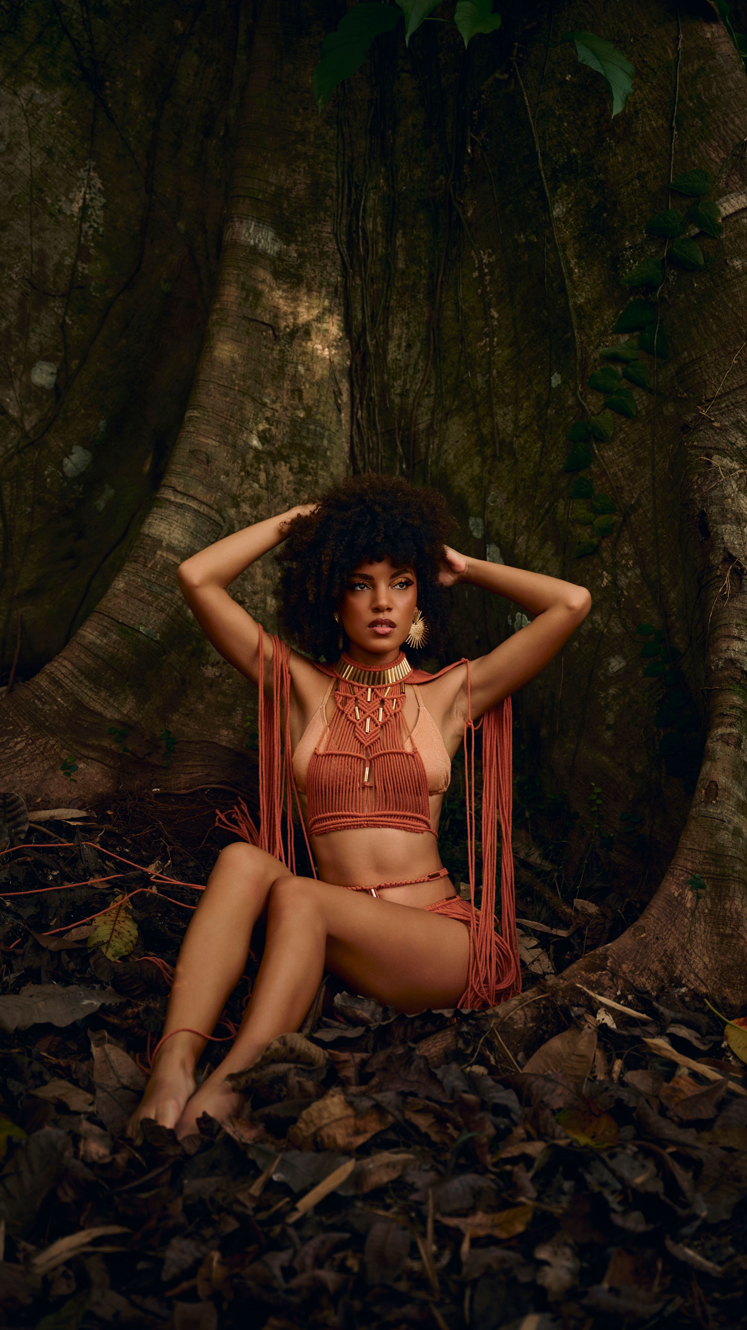 Artistic fashion portrait in moody forest setting with fringe details and brown earth tones among large tree roots.