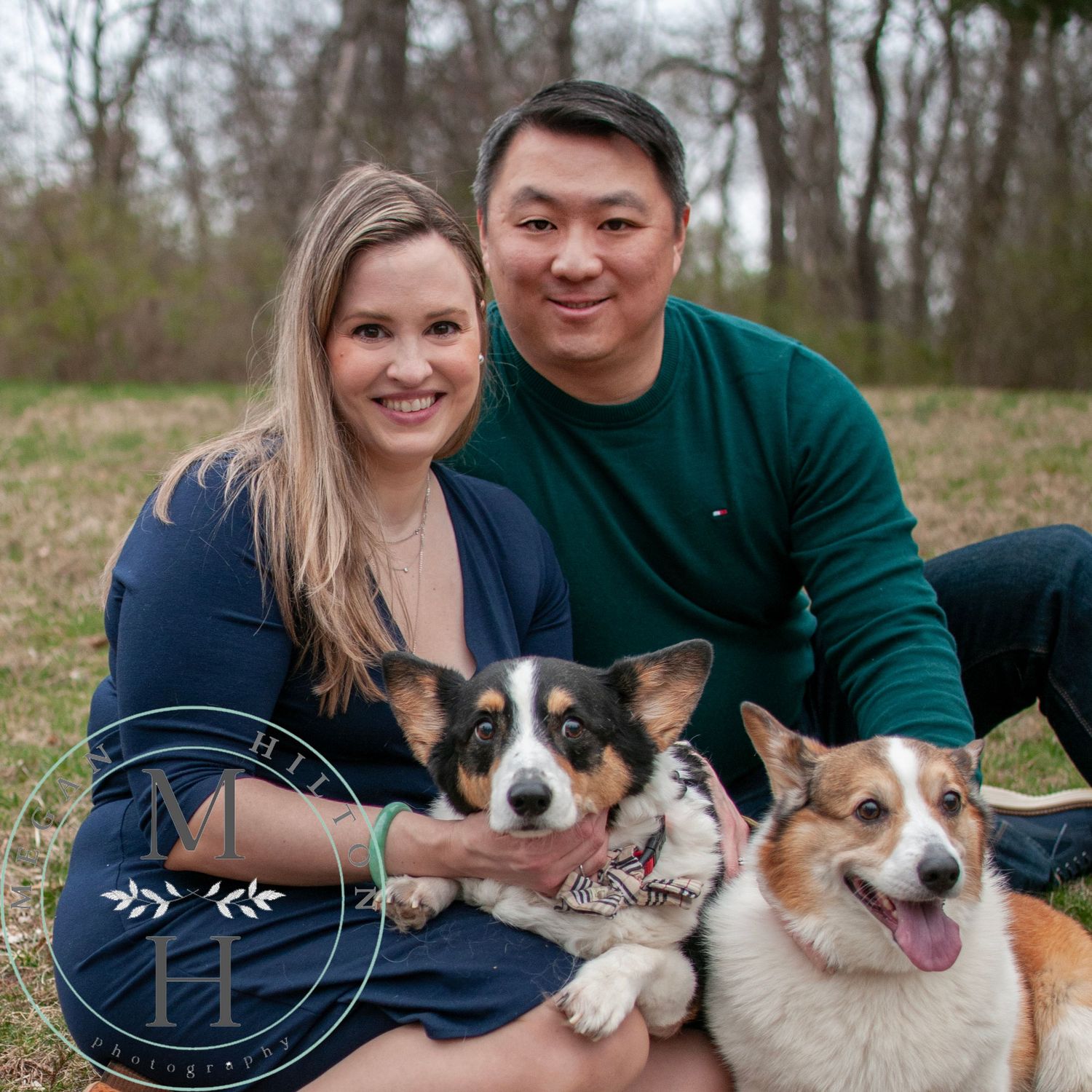 Couple sitting outdoors on grass with their two happy Corgi dogs.