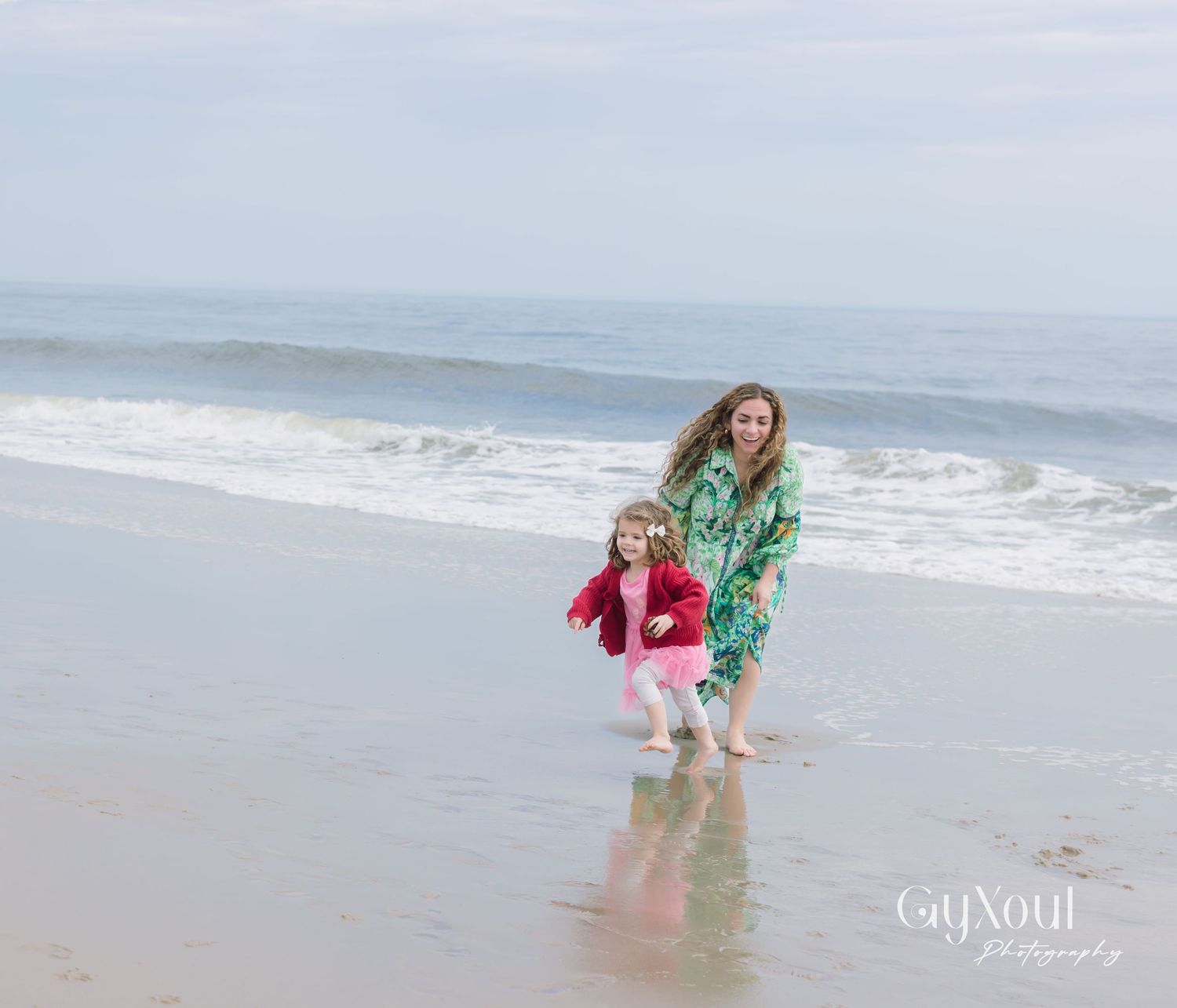 Two people enjoying a playful moment at the beach while waves roll in on a cloudy day.
