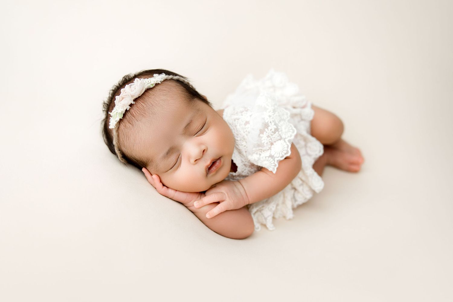 Sleeping Newborn baby girl in a lace dress on a cream backdrop
