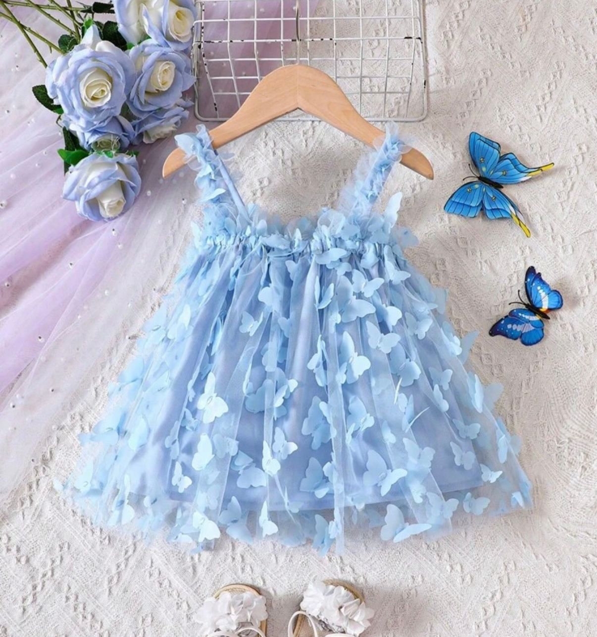 Light blue butterfly tulle dress with delicate details hanging on display.