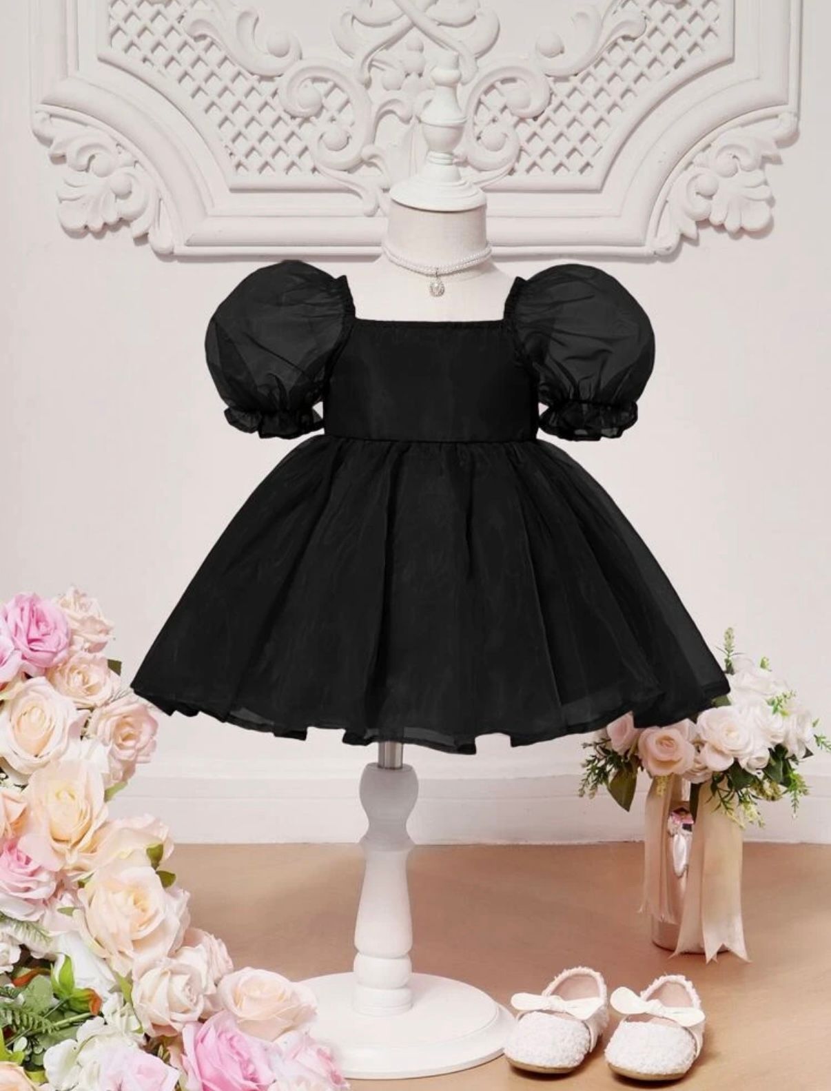 Black puff sleeve party dress with full skirt displayed on mannequin with floral decorations.