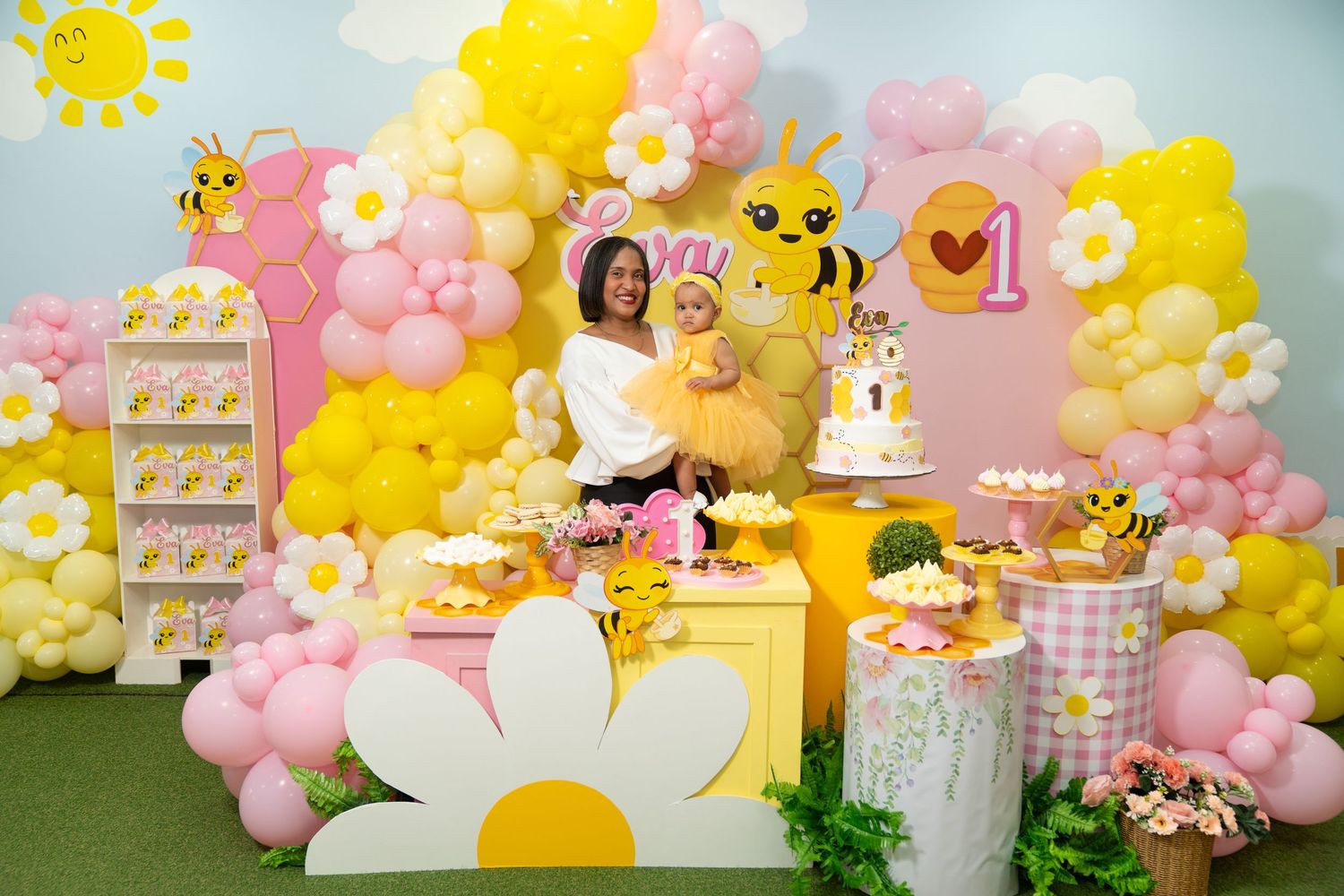 Whimsical bee-themed party setup with pink and yellow balloon garland, dessert table, and honey-inspired decorations.