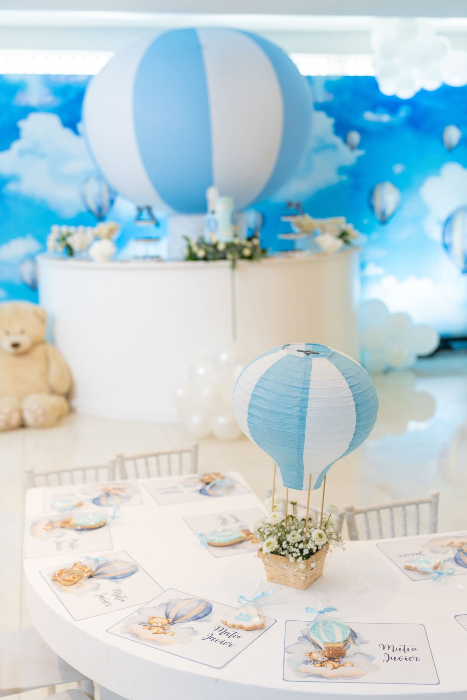 Baby shower party table decorated with blue hot air balloon centerpiece and cloud theme decor in white and blue colors.
