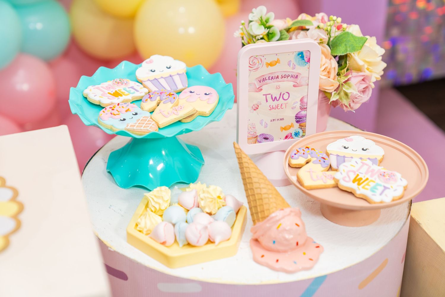 Colorful cookies and desserts displayed on white plates with pastel decorations and ice cream cone party theme details.