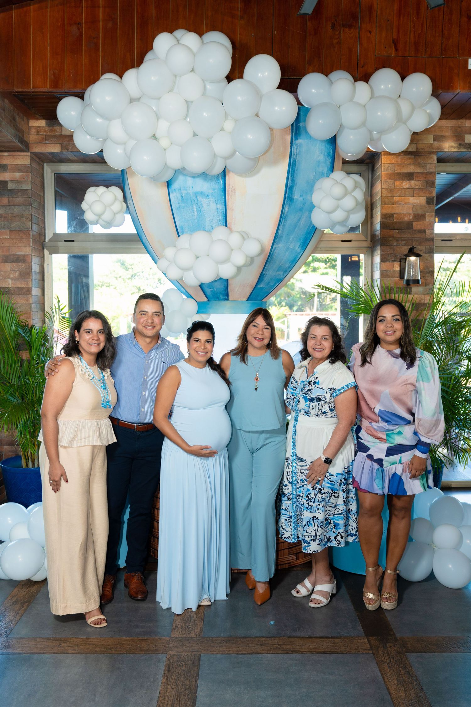 A group of people standing together at a baby shower celebration with white and blue balloon decorations in the background.