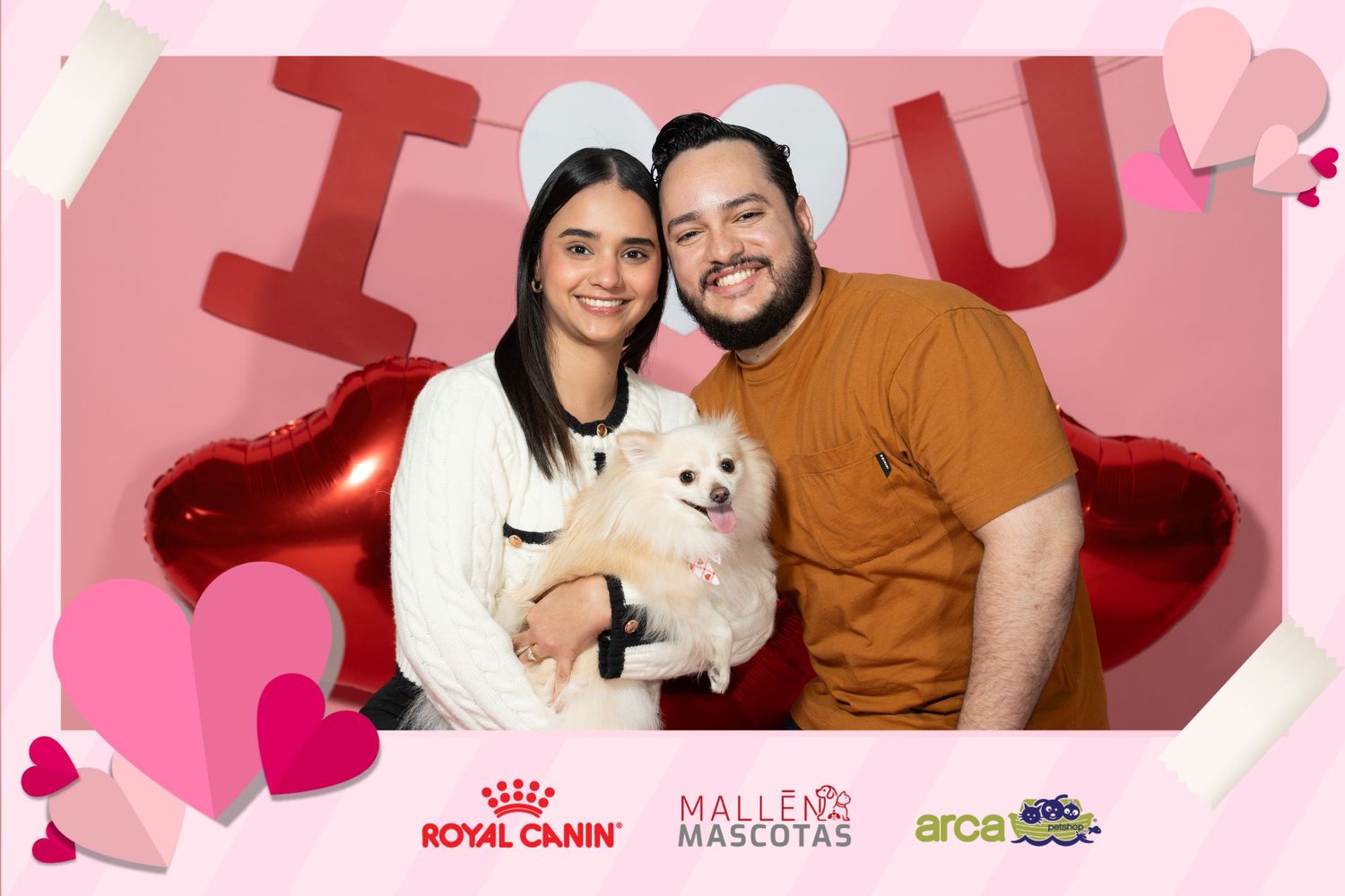 A couple poses together against a pink background with heart decorations and pet brand logos for a Valentine's themed photo.