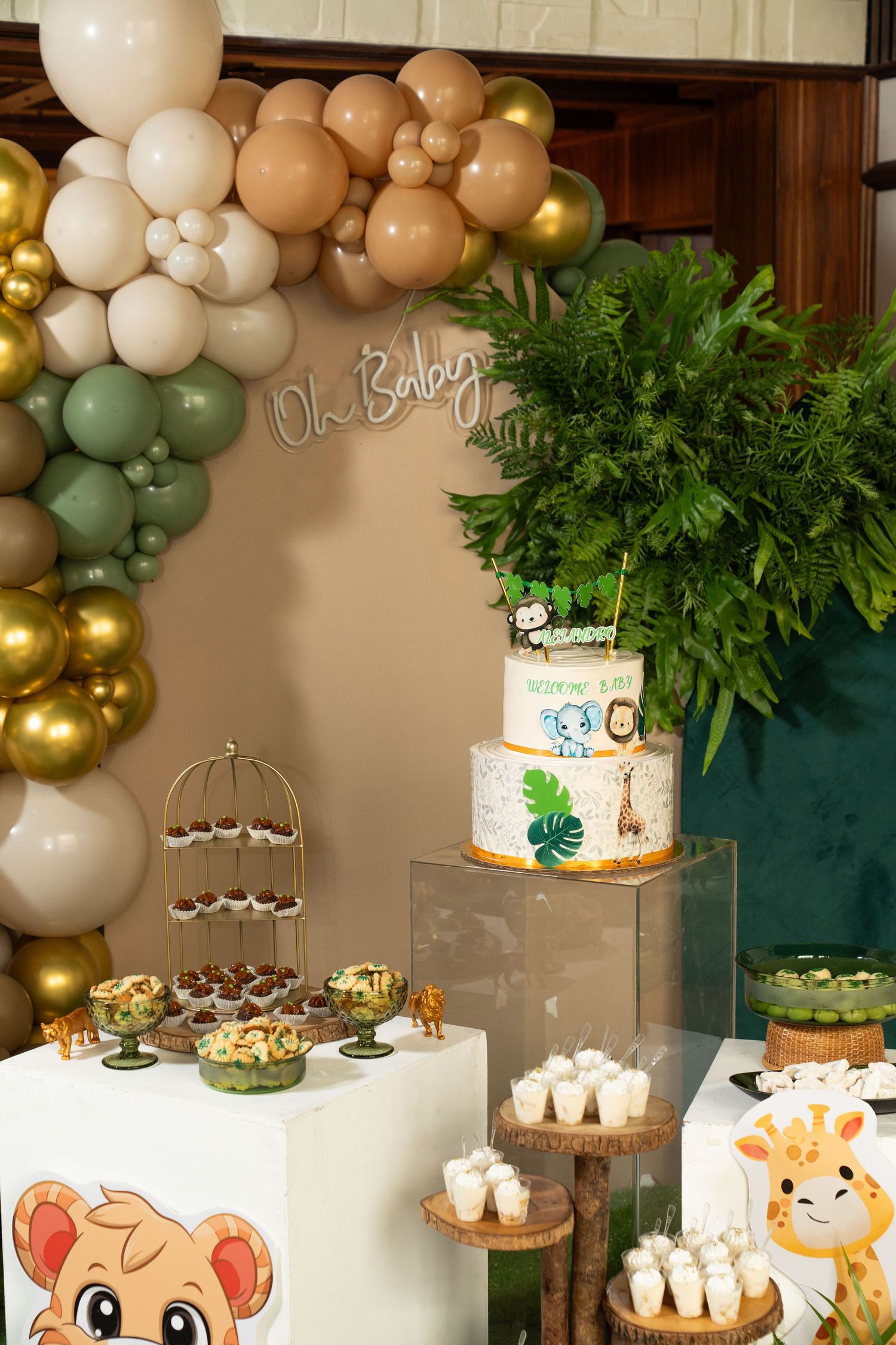 Baby shower dessert table decorated with balloon garland, cake, cupcakes and jungle animal themed decorations.