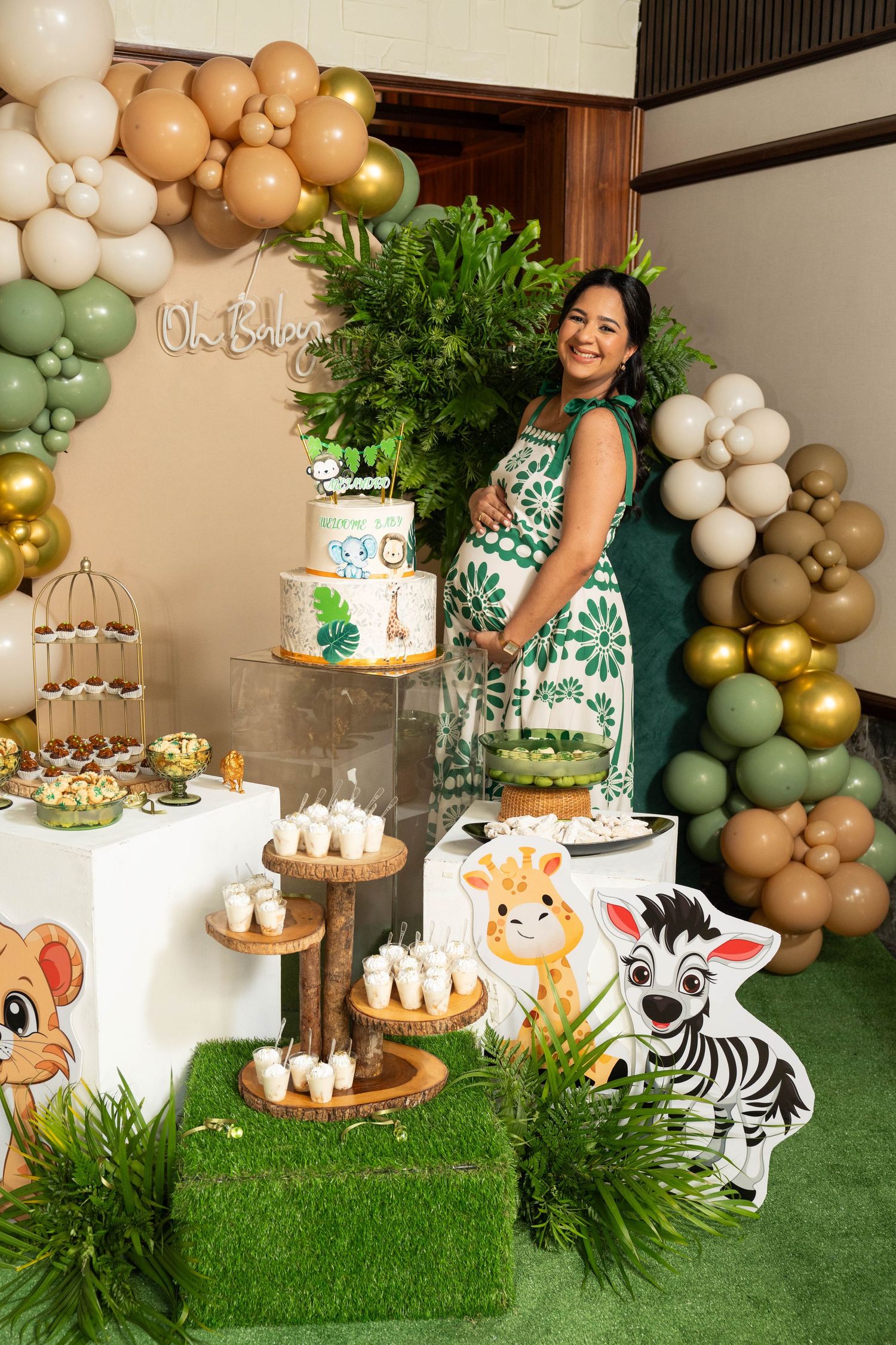 Safari themed party decoration with balloon arch, dessert table, artificial grass, and jungle animal cutouts.