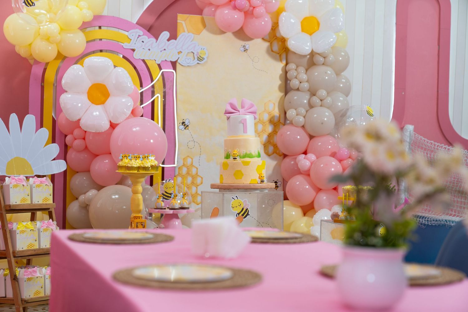 Pink and yellow balloon decorations adorn a pastel-themed party table setting with floral accents and table settings.