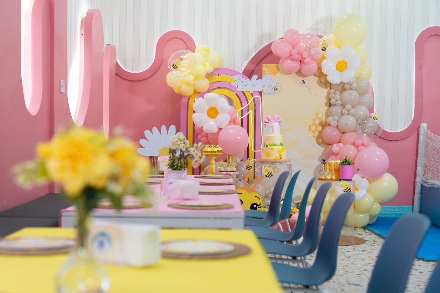 Colorful spring-themed party setup with floral centerpieces, pink decor, and blue chairs around dining tables.