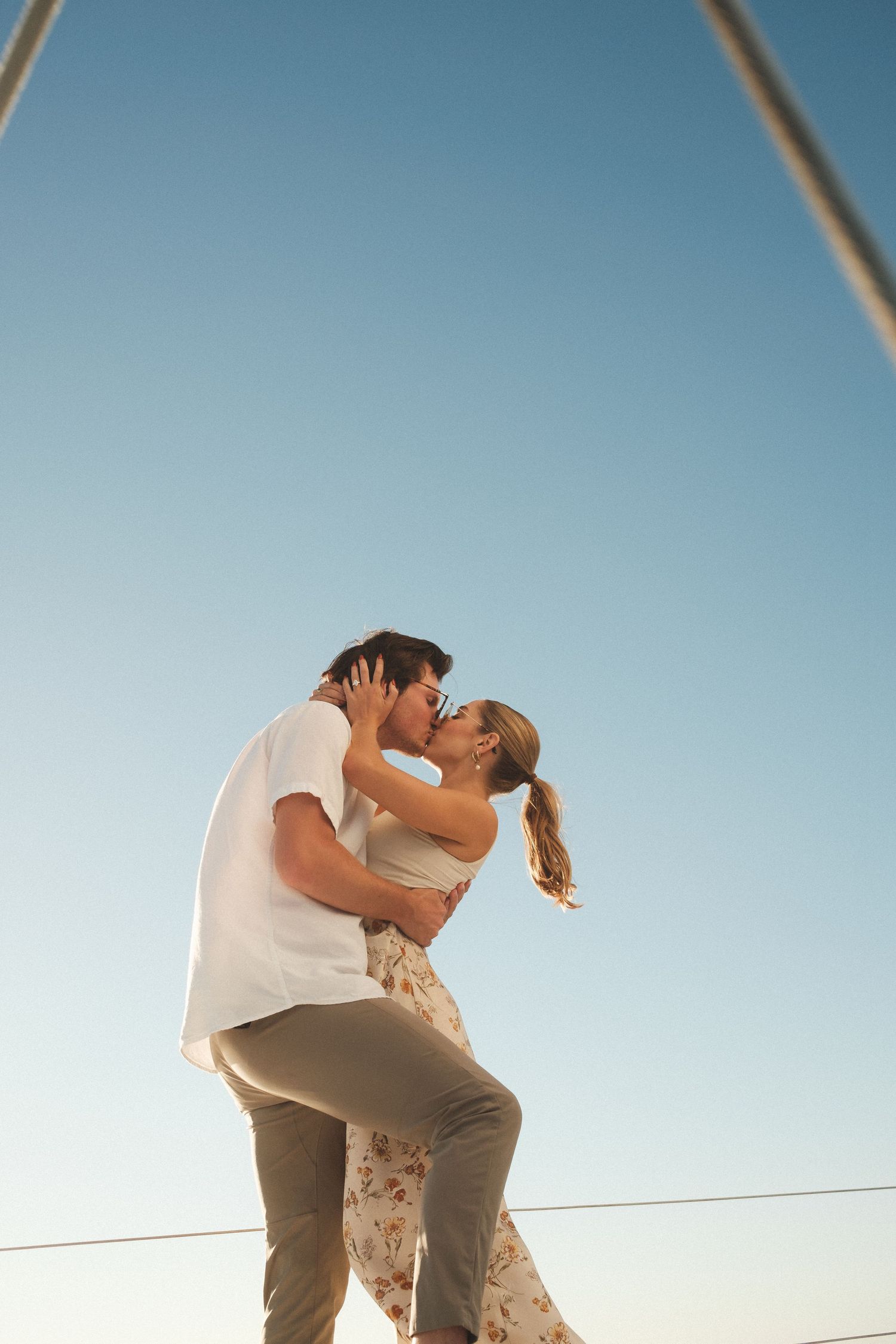 Couple sharing an intimate moment on a sailboat deck against a bright blue sky.