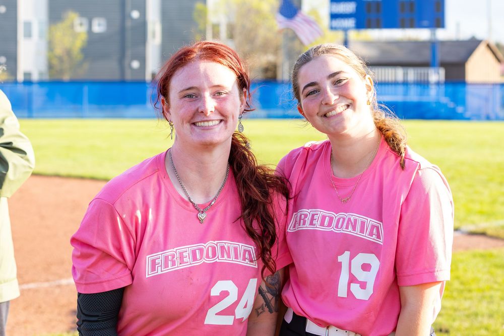 Players wearing pink jerseys pose together on softball field.