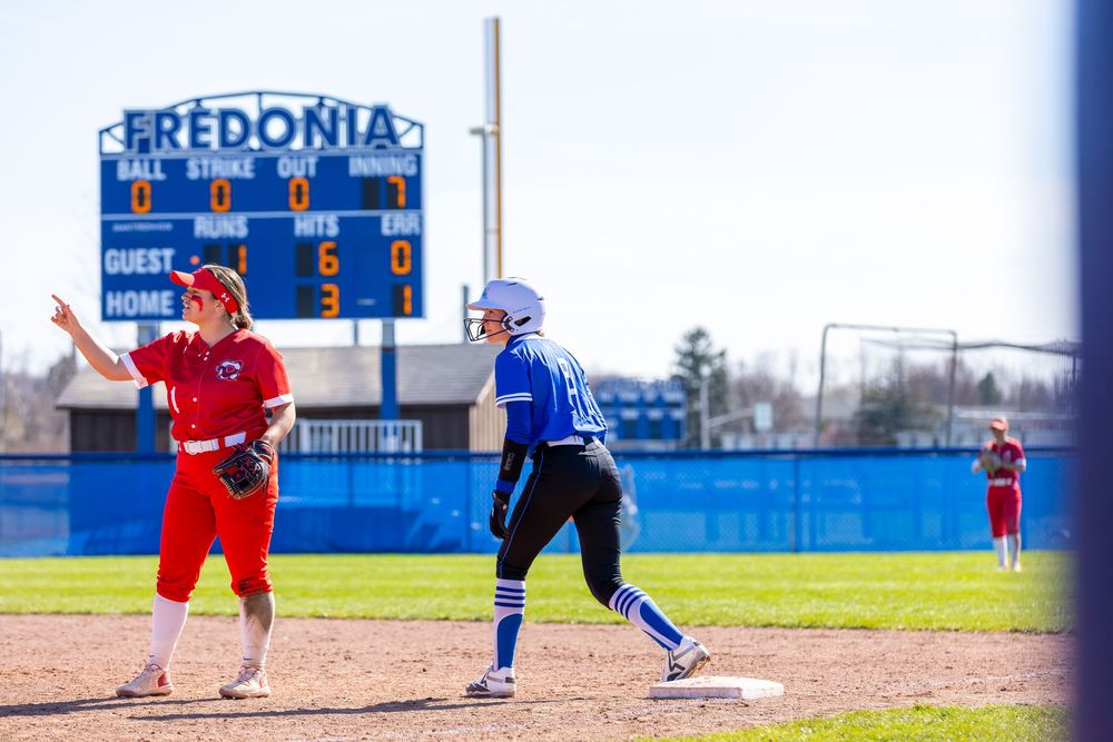 Softball game underway at Fredonia State field with scoreboard visible.