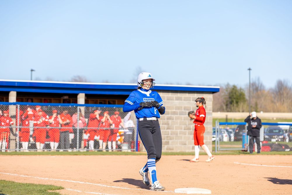 Spring softball game in progress with clear blue sky and spectators watching.