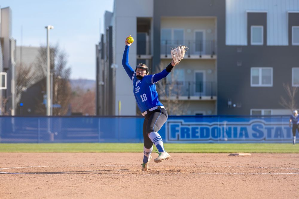 Softball action shot with Fredonia State signage visible in background.