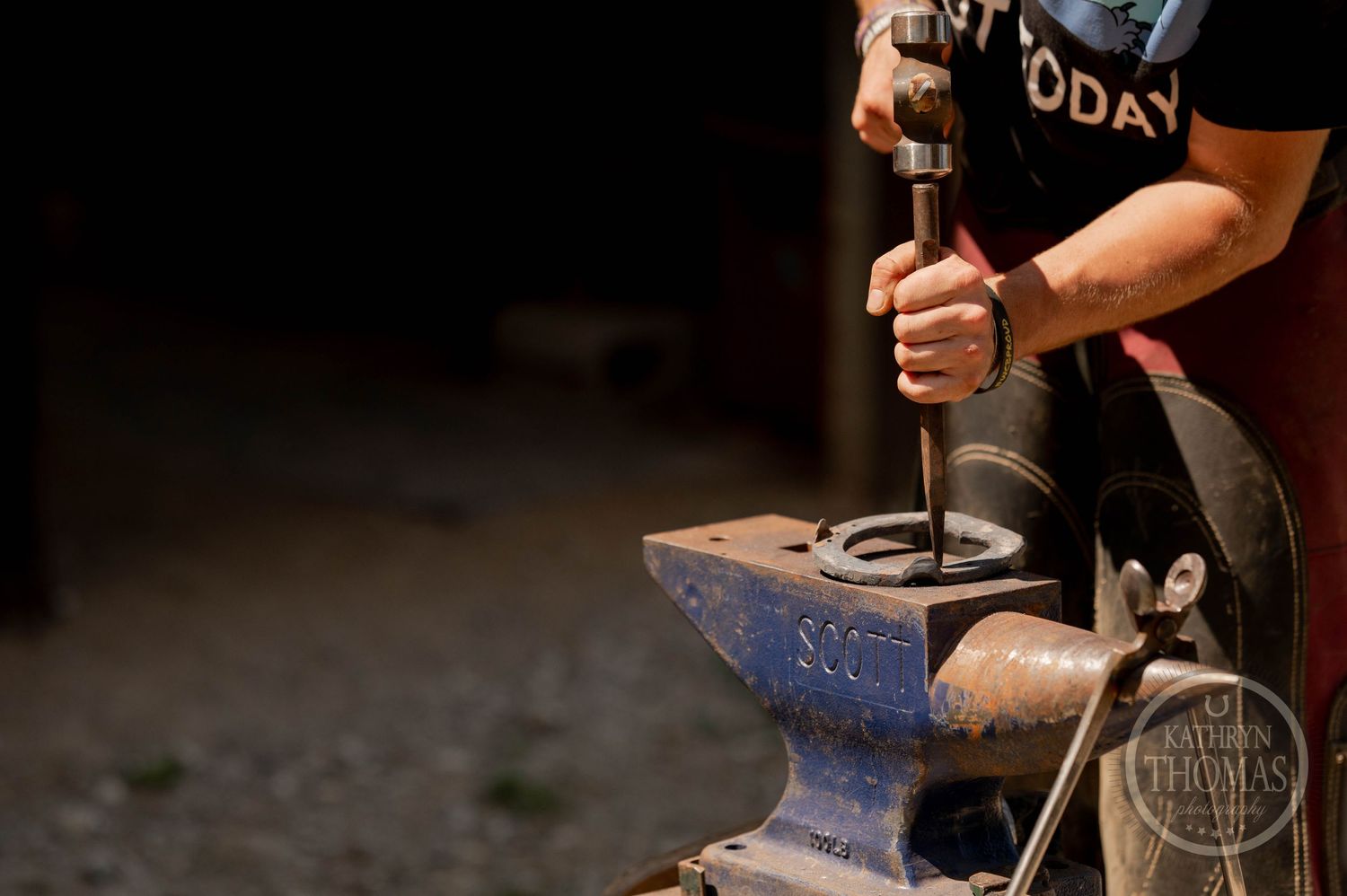 Person using tools on a blue Scout anvil in workshop lighting.