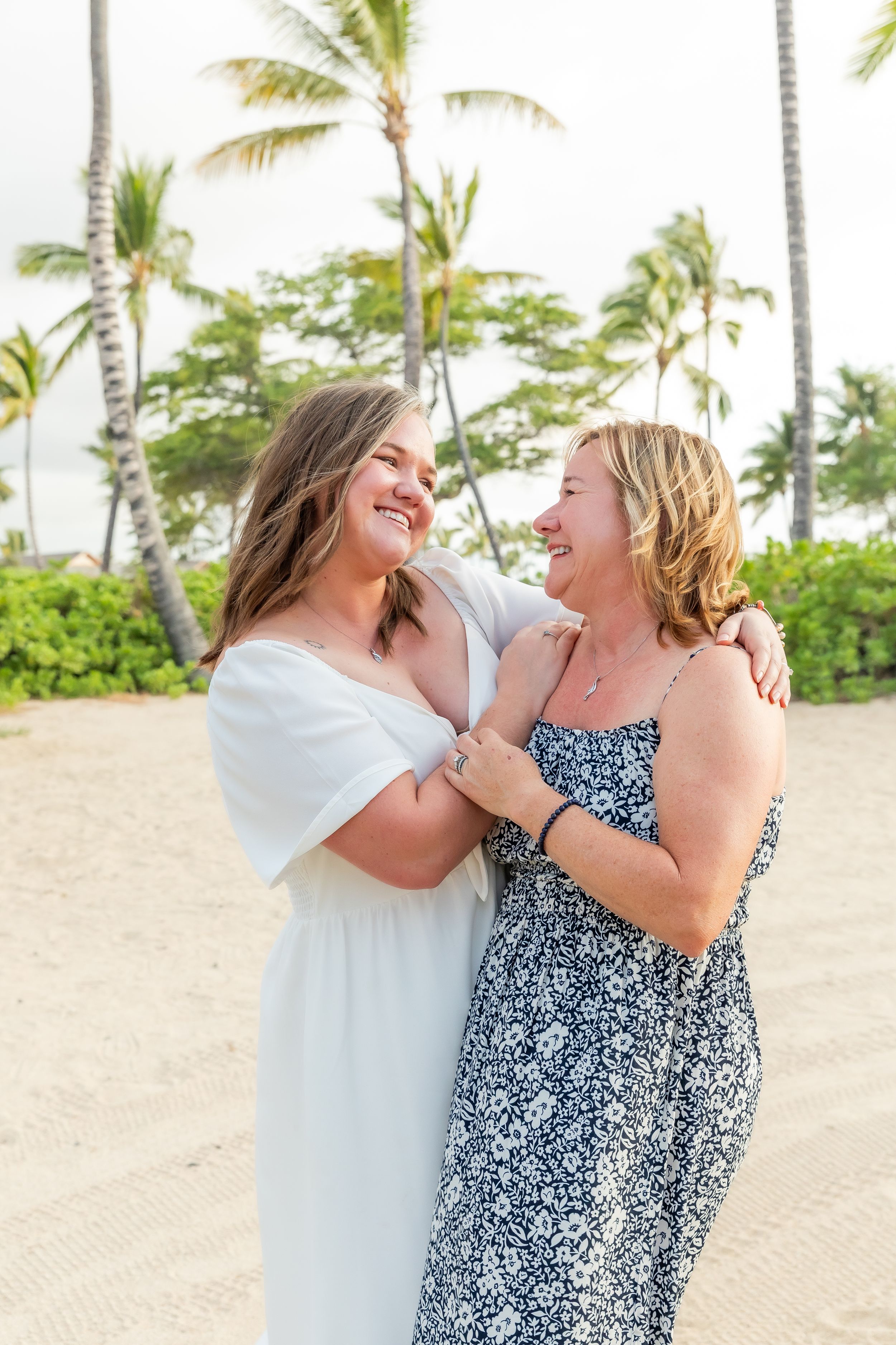 Two friends share a joyful moment laughing together on a tropical beach with palm trees swaying in the background.