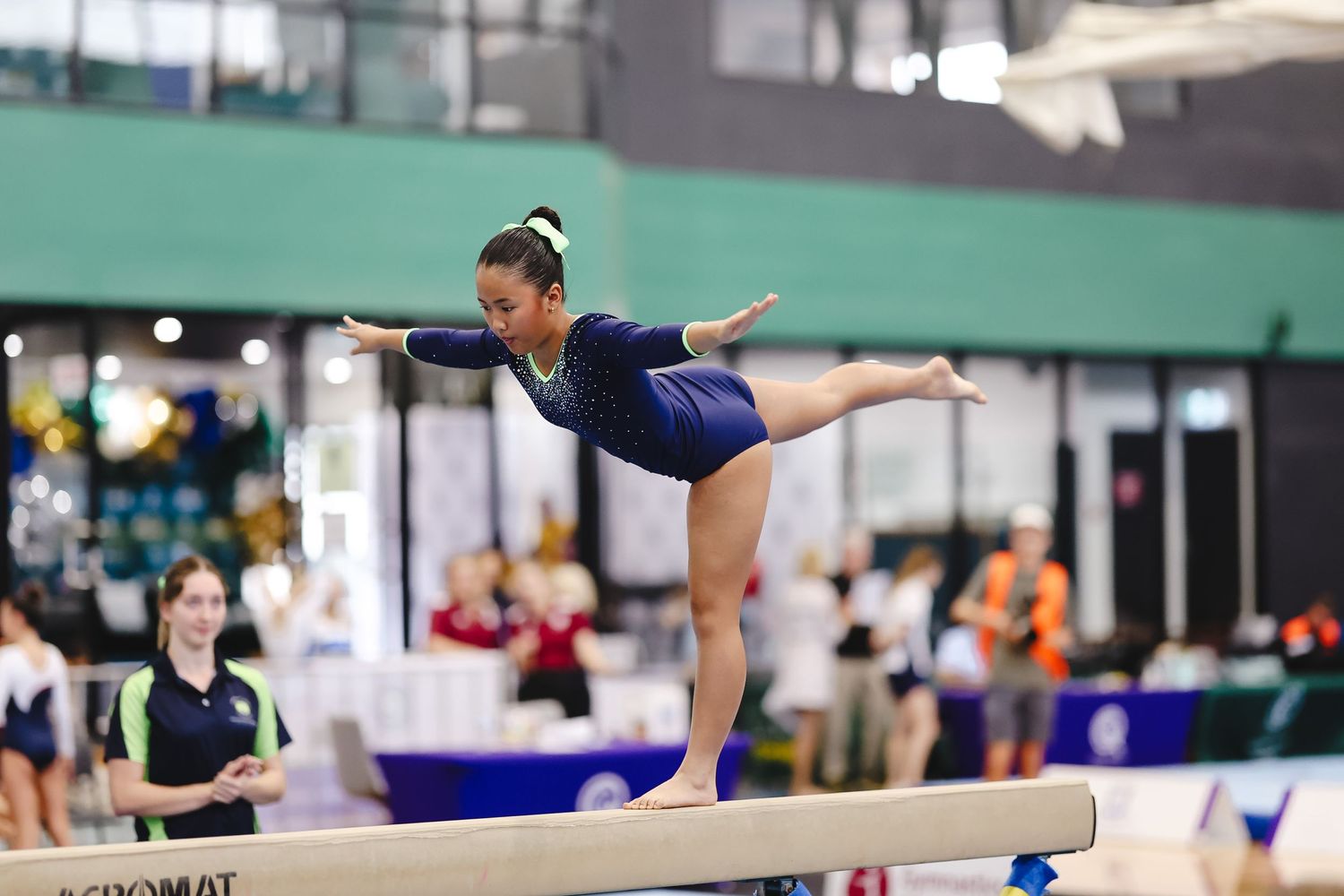 A gymnast performs a balance beam routine during a competition in a sports arena.