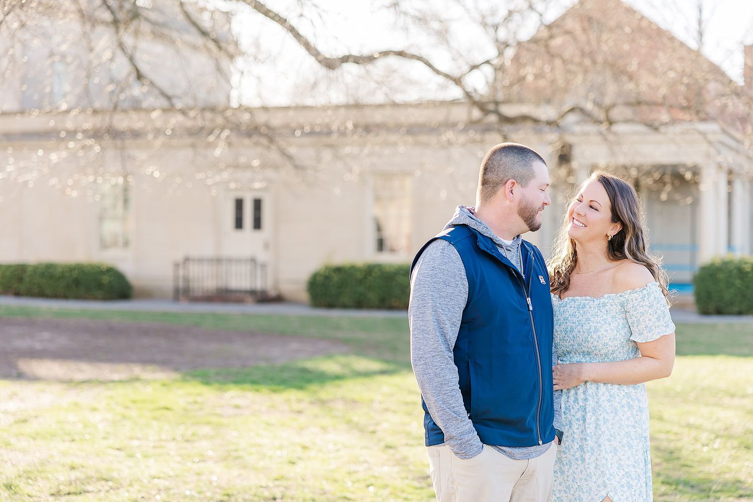A couple shares a romantic moment together outdoors in front of a neutral-toned building and green lawn.