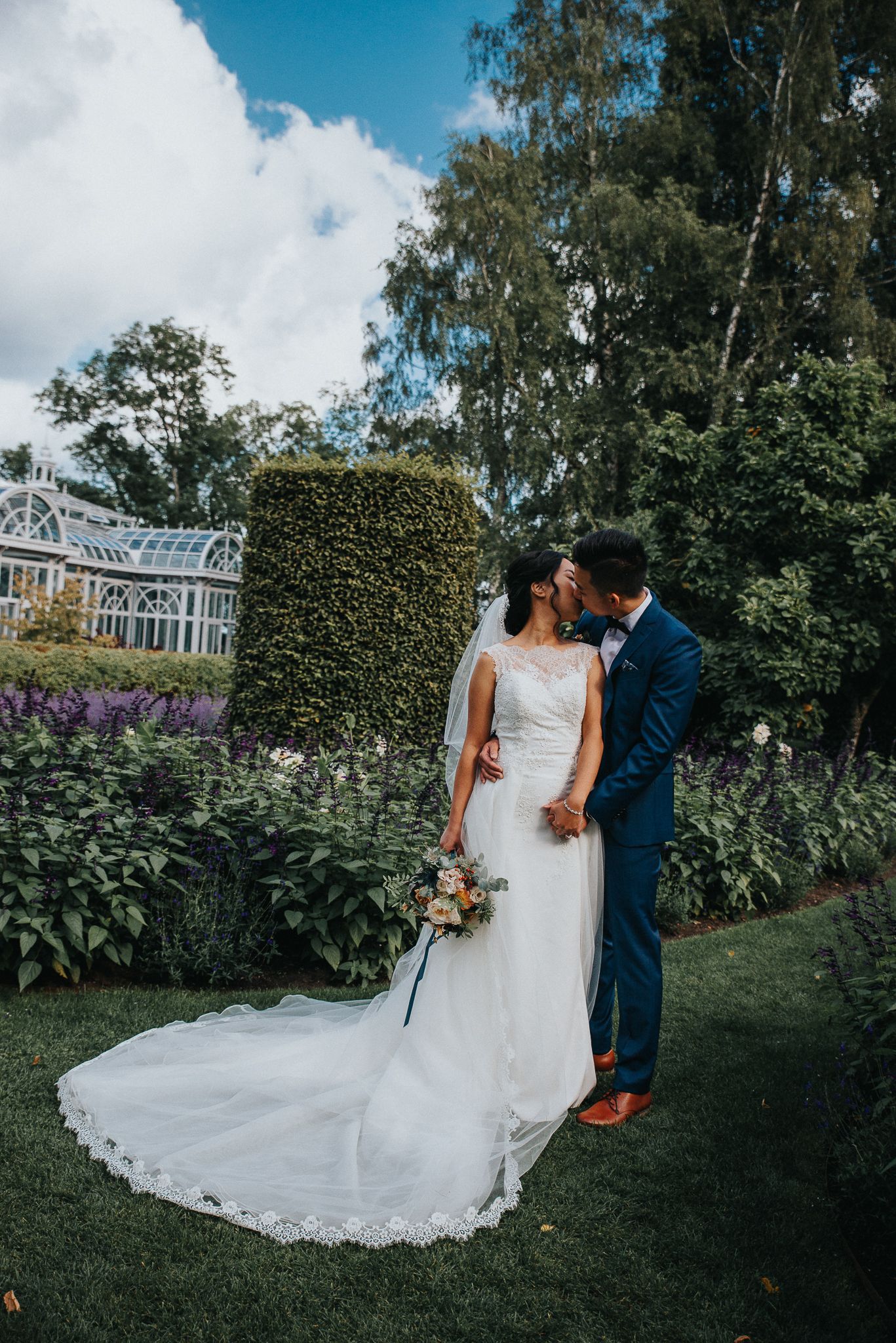 Elegant wedding portraits in a manicured garden with white dress and navy suit against floral backdrop.