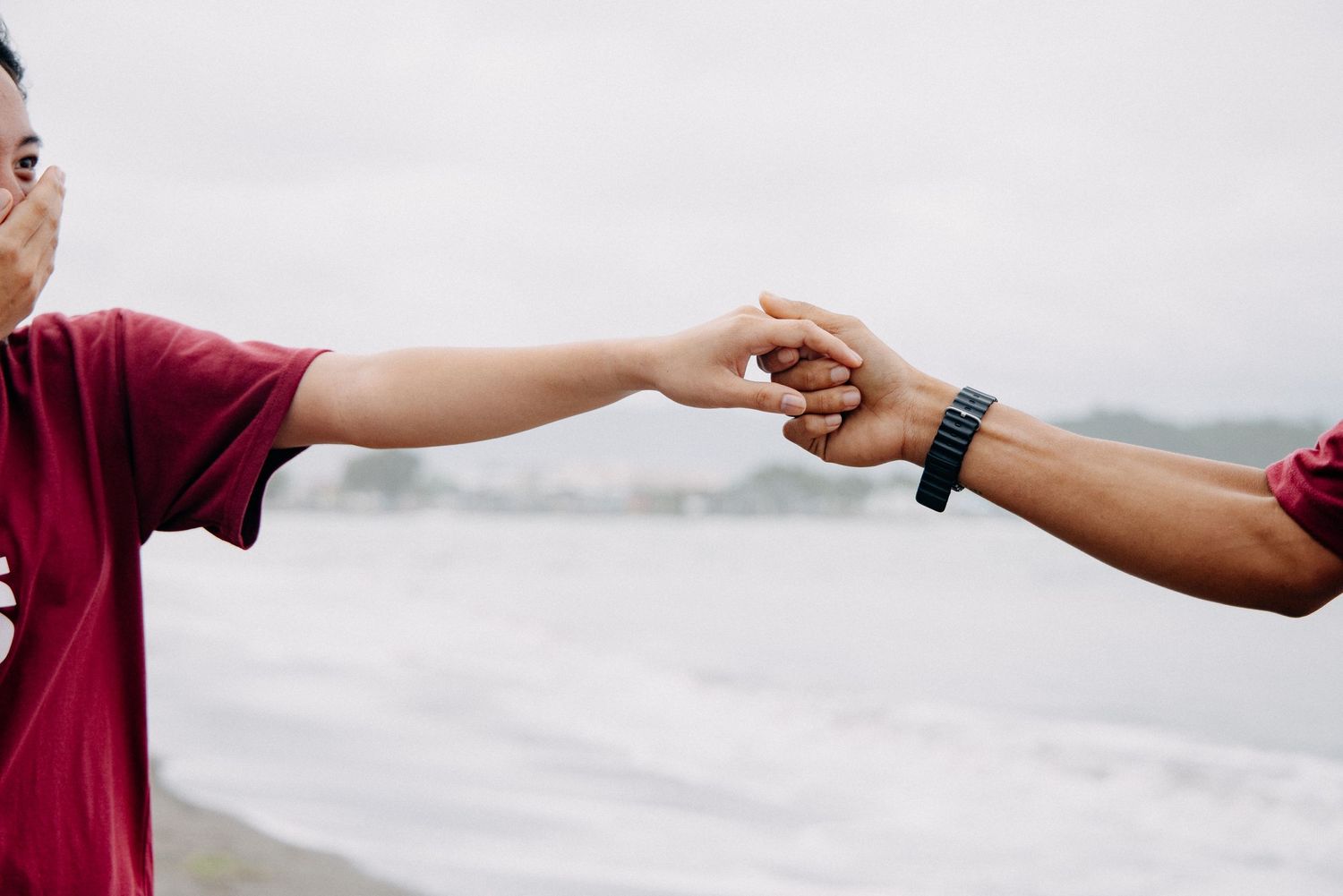 Two people reaching out to hold hands against a bright sky background.