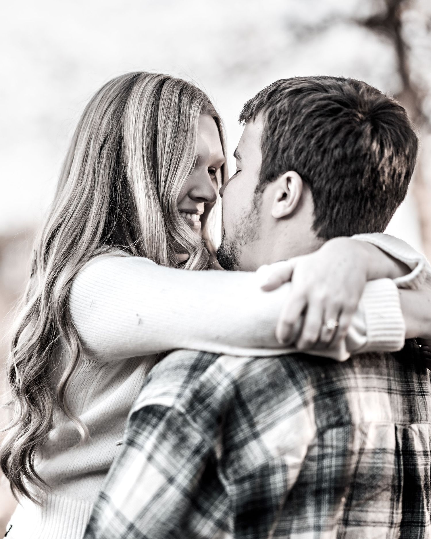 A couple embraces and laughs together in black and white, with the person wearing a plaid flannel shirt.