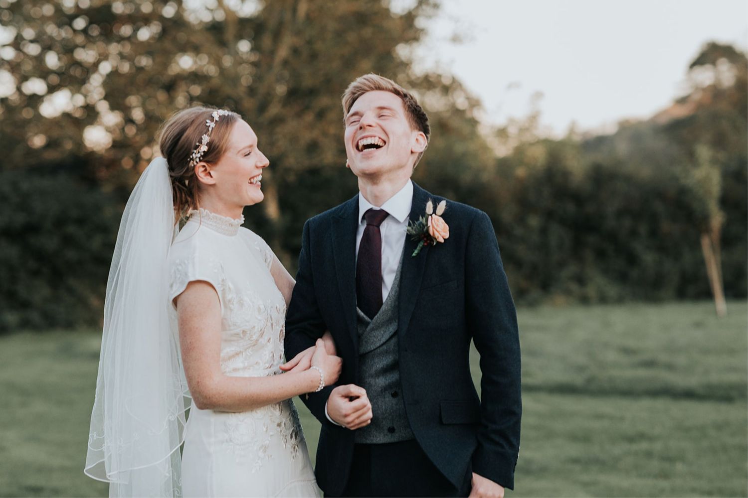 A joyful bride and groom share a candid laughing moment together in a garden setting during golden hour.