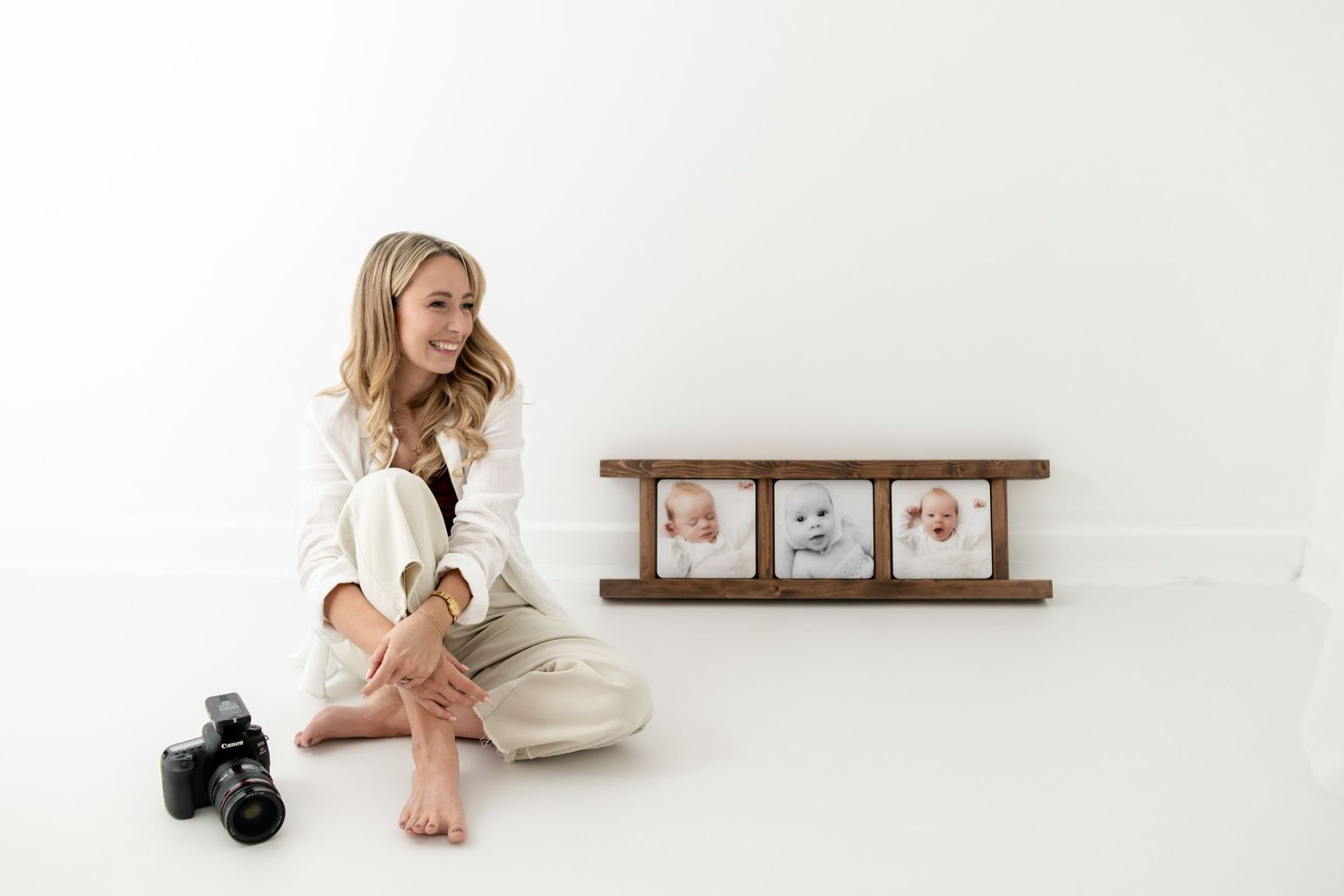 A photographer sits in a minimalist white studio setting with artwork on shelf and camera equipment nearby.
