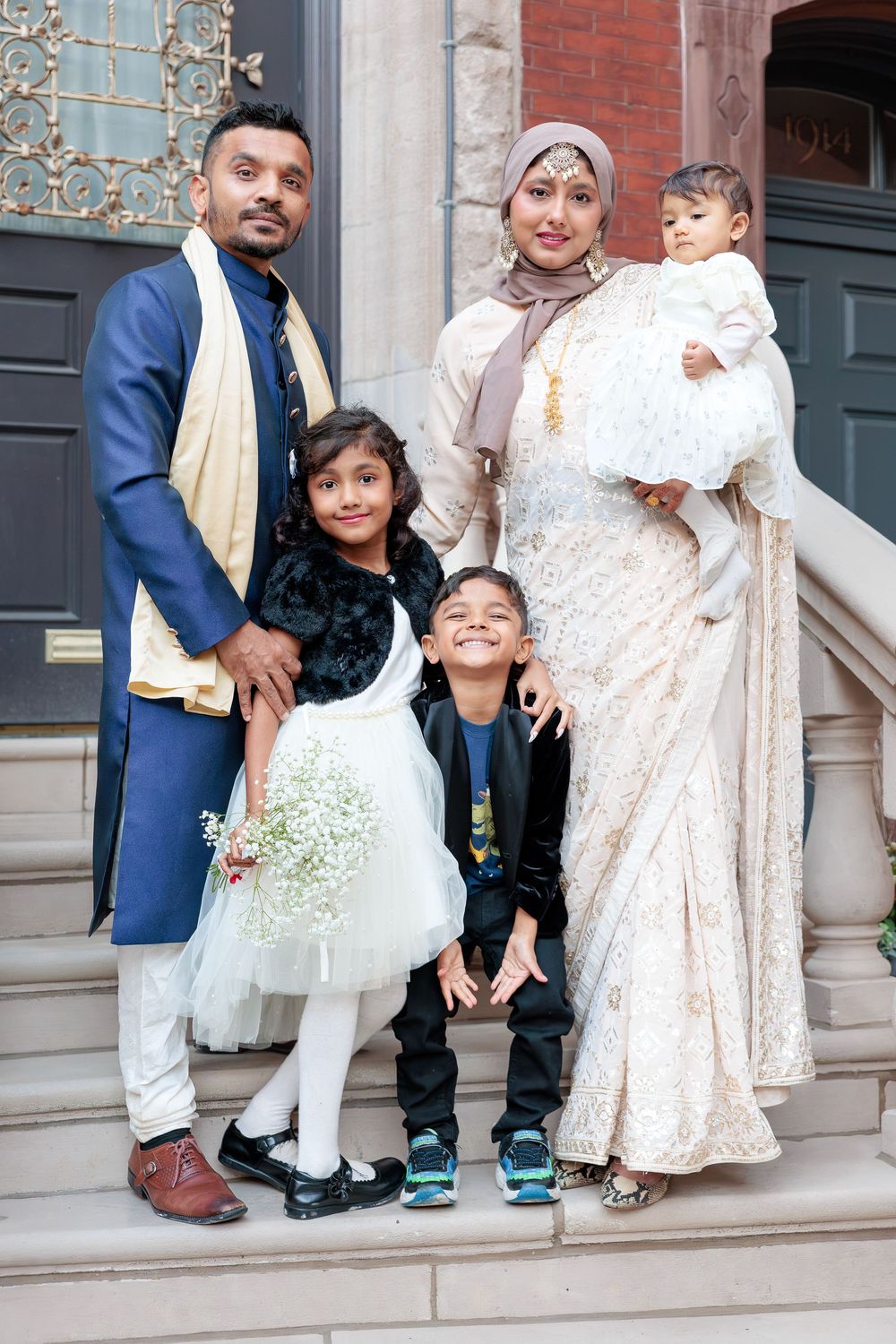 South Asian family in traditional attire posing on steps with two children and a baby.
