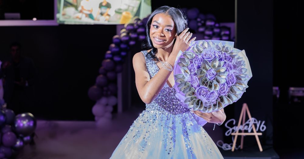 A young girl in a blue quinceañera gown holds a large purple money bouquet at her Sweet 16 party.